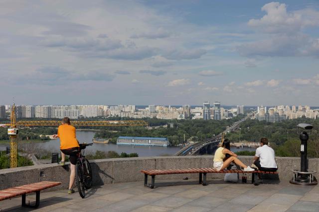 People sit on a bench and look at the city in Kyiv on June 24, 2026, amid the Russian invasion of Ukraine. (Photo by Tetiana DZHAFAROVA / AFP)