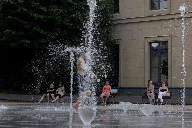 Women sit on a bench by a fountain in Kyiv on June 24, 2026, amid the Russian invasion of Ukraine. Europe struggled to cope with a record-breaking heatwave on June 24, 2026, with at least 94 million people expected to experience temperatures above 35C, most of them in France and Spain. (Photo by Tetiana DZHAFAROVA / AFP)