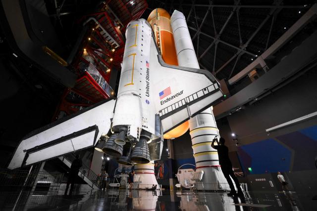 People take pictures underneath NASA’s Space Shuttle Endeavour as it stands stacked complete in a launch-ready vertical display with the ET-94 External Fuel Tank and a pair of Solid Rocket Boosters (SRBs) inside the Samuel Oschin Shuttle Gallery at the California Science Center in Los Angeles, on June 24, 2026. The Space Shuttle Endeavour exhibit will open on November 13, 2026 as part of a 200,000-square-foot expansion with the Samuel Oschin Air and Space Center. (Photo by Patrick T. Fallon / AFP)