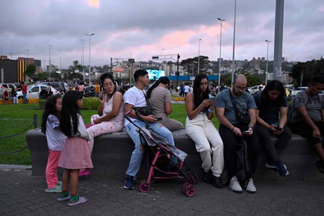 People use thier mobile phones as they remain in the street following an earthquake in Caracas on June 24, 2026. A magnitude 7.1 earthquake struck Venezuela on Wednesday, the United States Geological Survey (USGS) reported, triggering panic in Caracas, according to AFP journalists. The tremor, which was followed by several aftershocks, was also felt in Colombia. (Photo by Federico PARRA / AFP)