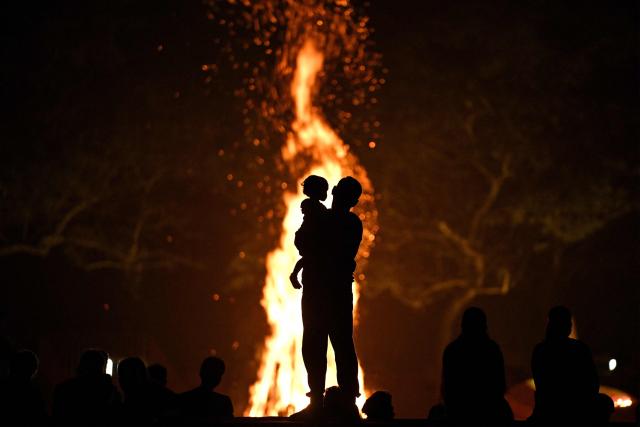 This photograph taken on February 28, 2026 shows residents and visitors standing around a bonfire in front of the Matri Mandir during a celebration marking the anniversary of the founding of Auroville near Puducherry. For decades Auroville held fast to its lofty ideals as a self-governing haven for yoga enthusiasts and seekers of spiritual freedom of "all creeds and all nationalities". Until India's Hindu nationalist prime minister Narendra Modi turned his attention to the lush paradise its founders created on an once arid plateau Puducherry. Those most at risk are the half of Auroville's 3,300 residents who were born abroad, and who now live in fear of being expelled or denied visas to remain. (Photo by Idrees MOHAMMED / AFP)