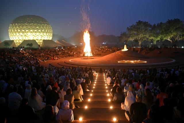 This photograph taken on February 28, 2026 shows residents and visitors attending a bonfire celebration in front of the Matri Mandir (L), marking the anniversary of the founding of Auroville near Puducherry. For decades Auroville held fast to its lofty ideals as a self-governing haven for yoga enthusiasts and seekers of spiritual freedom of "all creeds and all nationalities". Until India's Hindu nationalist prime minister Narendra Modi turned his attention to the lush paradise its founders created on an once arid plateau Puducherry. Those most at risk are the half of Auroville's 3,300 residents who were born abroad, and who now live in fear of being expelled or denied visas to remain. (Photo by Idrees MOHAMMED / AFP)