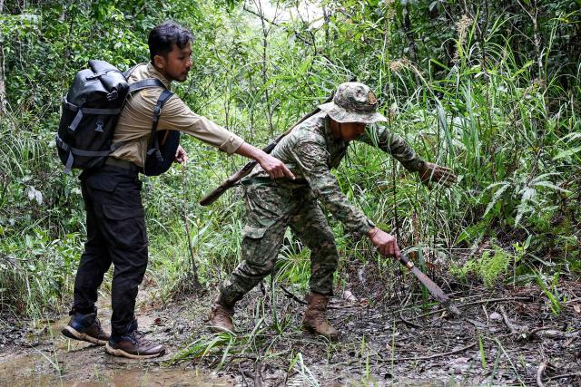 This photo taken on June 9, 2026 shows Chea Sareach (L), Biodiversity and Science Senior Coordinator of Conservation International Cambodia, and ranger Hou Sophoan (C) looking at an animal footprint in the Cardamom National Park in Koh Kong province. Above the patter of rain cascading through the jungle canopy comes the haunting call of a pileated gibbon singing to fend off intruders in Cambodia's Cardamom Mountains. (Photo by TANG CHHIN Sothy / AFP) / To go with 'CAMBODIA-CONSERVATION-ENVIRONMENT-ANIMAL-SCIENCE-FORESTS,FOCUS' by Sara HUSSEIN and Suy SE