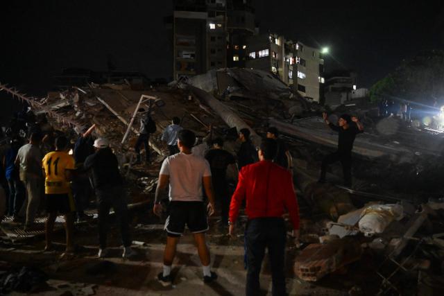 People stand next to a collapsed building following an earthquake in Caracas on June 24, 2026. Two earthquakes of magnitude 7.2 and 7.5 struck the same area of Venezuela on the evening of June 24, causing buildings to collapse, according to the United States Geological Survey (USGS) and AFP journalists. The quakes drove residents of the capital, Caracas, into the streets. (Photo by Juan BARRETO / AFP)
