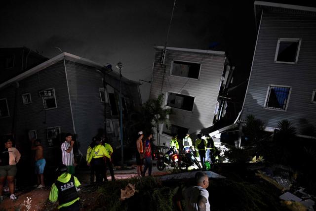 Residents and emergency workers stand near damaged buildings following an earthquake in Catia La Mar, La Guaira state, some 30kms north-west of Caracas, early on June 25, 2026. Powerful twin earthquakes have killed 32 people and injured more than 700, the nation's interim president said on June 25, after the massive shocks collapsed entire buildings and sent people running in panic. (Photo by Federico PARRA / AFP)