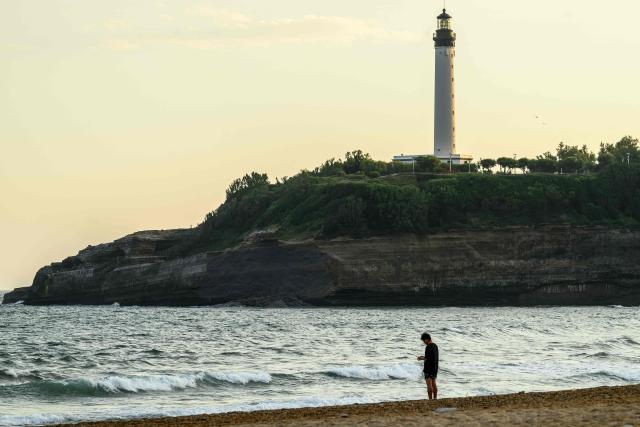 A man stands in front of the cliff near Miramar beach, below the Biarritz lighthouse, on the morning after the cliff collapse, in Biarritz, south-western France, on June 25, 2026. A section of cliff approximately 2,000 square metres in size fell into the sea on the evening of June 24. The body of one victim was found, authorities said shortly before 11 pm, while another person was still missing. (Photo by Philippe LOPEZ / AFP)