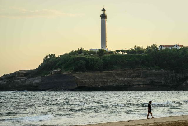A man stands in front of the cliff near Miramar beach, below the Biarritz lighthouse, on the morning after the cliff collapse, in Biarritz, south-western France, on June 25, 2026. A section of cliff approximately 2,000 square metres in size fell into the sea on the evening of June 24. The body of one victim was found, authorities said shortly before 11 pm, while another person was still missing. (Photo by Philippe LOPEZ / AFP)