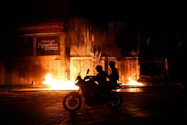 A motorcyclist drives past a fire outside a building following an earthquake in Catia La Mar, La Guaira state, some 30kms north-west of Caracas, early on June 25, 2026. Powerful twin earthquakes have killed 32 people and injured more than 700, the nation's interim president said on June 25, after the massive shocks collapsed entire buildings and sent people running in panic. (Photo by Federico PARRA / AFP)