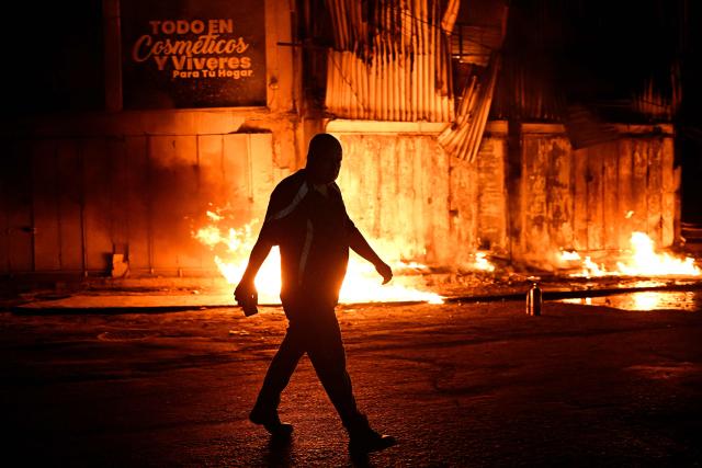 A man walks past a fire outside a building following an earthquake in Catia La Mar, La Guaira state, some 30kms north-west of Caracas, early on June 25, 2026. Powerful twin earthquakes have killed 32 people and injured more than 700, the nation's interim president said on June 25, after the massive shocks collapsed entire buildings and sent people running in panic. (Photo by Federico PARRA / AFP)