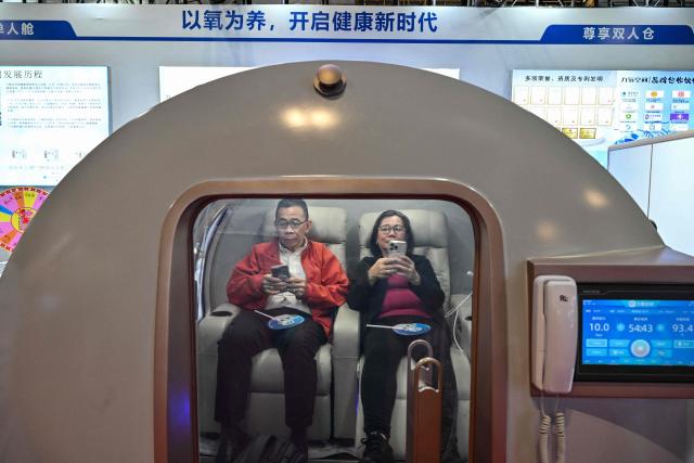 A couple is seen inside a micro hyperbaric oxygen chamber during the 2026 Shanghai International Medical Devices Exhibition in Shanghai on June 25, 2026. (Photo by HECTOR RETAMAL / AFP)
