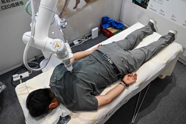A man lying on a massage table receives a massage from an AI-powered robot during the 2026 Shanghai International Medical Devices Exhibition in Shanghai on June 25, 2026. (Photo by HECTOR RETAMAL / AFP)