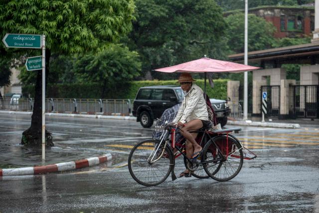 A trishaw driver and his passenger use umbrellas to cover from the rain in Yangon on June 25, 2026. (Photo by Sai Aung MAIN / AFP)