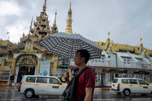 A man walks with an umbrella to shield himself from the rain as he walks past Sule Pagoda in Yangon on June 25, 2026. (Photo by Sai Aung MAIN / AFP)
