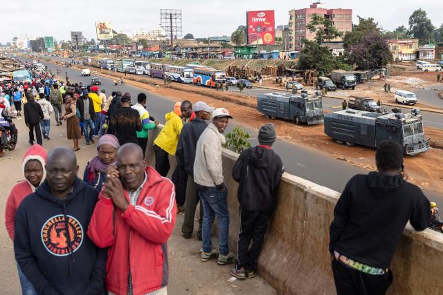 People watch Kenyan police officers at a roadblock in the Central Business District (CBD) in the Kangemi neighbourhood ahead of the planned demonstrations to mark the second anniversary of the deadly June 2024 youth-led anti-Finance Bill protests, which saw demonstrators storm Parliament, in Nairobi on June 25, 2026. Thousands of Kenyans protested in June 2024 against economic hardship and corruption, eventually storming parliament to force the cancellation of new taxes. (Photo by Tony KARUMBA / AFP)