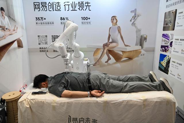 A man receives a massage from an AI-powered robot during the Shanghai International Medical Devices Exhibition in Shanghai on June 25, 2026. (Photo by HECTOR RETAMAL / AFP)