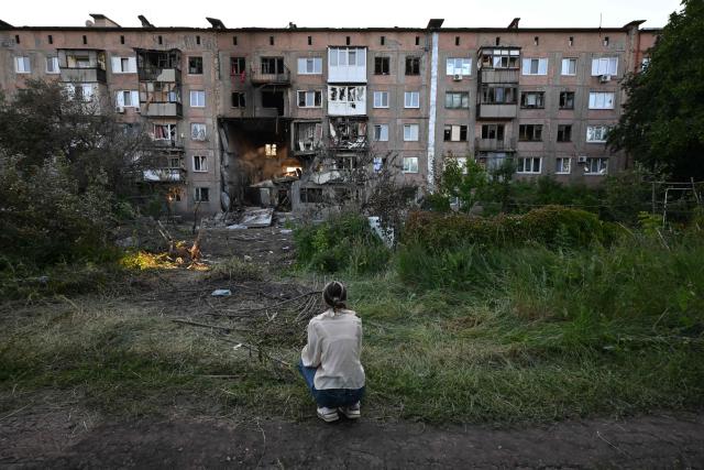 A girl sits in front of a heavily damaged multi-storey apartment building following a recent attack, which local Russian-installed officials called a Ukrainian drone strike, in the town of Gorlivka in the Donetsk region, Russian-controlled Ukraine, on June 24, 2026, amid the ongoing Russian-Ukrainian conflict. (Photo by AFP)