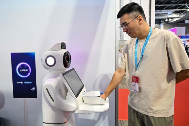 A man shows a robot that makes traditional Chinese medicine diagnoses during the Shanghai International Medical Devices Exhibition in Shanghai on June 25, 2026. (Photo by HECTOR RETAMAL / AFP)