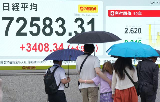 Pedestrians walk past an electronic quotation board displaying the Nikkei Stock Average on the Tokyo Stock Exchange along a street in Tokyo on June 25, 2026. (Photo by Kazuhiro NOGI / AFP)
