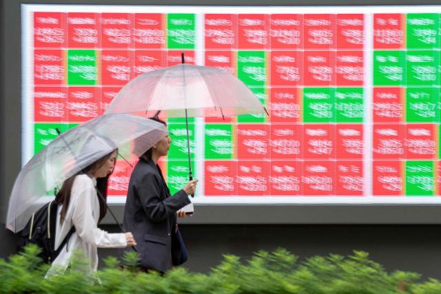 Pedestrians walk past an electronic quotation board displaying the Nikkei 225 stock prices on the Tokyo Stock Exchange along a street in Tokyo on June 25, 2026. (Photo by Kazuhiro NOGI / AFP)