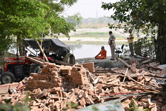 A police personnel stands guard as a Hindu holy man sits at a demolition site in a residential area along the banks of river Yamuna in New Delhi on June 25, 2026. (Photo by Arun SANKAR / AFP)