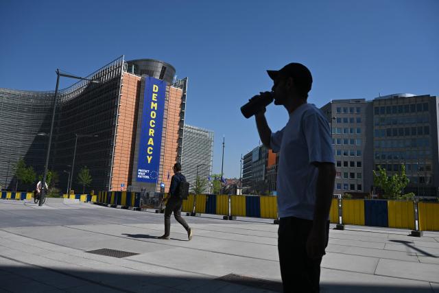 A man drinks water from a bottle as he stands in the shade near the European Commission building during a heatwave in Brussels on June 25, 2026. (Photo by Nicolas TUCAT / AFP)