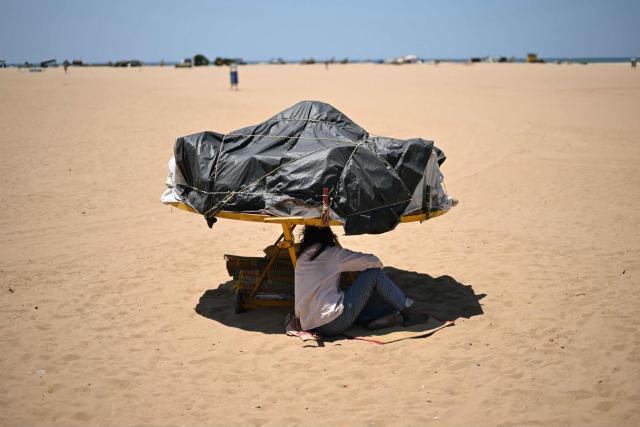 A man sits under the shade of a merry-go-round at Marina beach in Chennai on June 25, 2026. (Photo by R.Satish BABU / AFP)