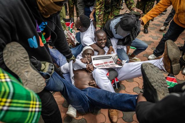 Protesters react as they try to resist while being arrested by Kenyan police officers outside Parliament buildings during demonstrations marking the second anniversary of the deadly June 2024 youth-led anti-Finance Bill protests, which saw demonstrators storm Parliament, in Nairobi on June 25, 2026. Kenyan police put on a massive show of force on June 25 in a bid to prevent protests marking two years since a landmark Gen Z uprising. Thousands of Kenyans took to the streets in June 2024 against economic hardship and corruption, eventually storming parliament to force the cancellation of new taxes. (Photo by Luis TATO / AFP)