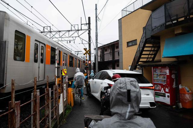 A train passes at a crossing on a small road as people wait in the rain to cross in Itabashi Ward in north Tokyo, on June 25, 2026. (Photo by ANDREW CABALLERO-REYNOLDS / AFP)