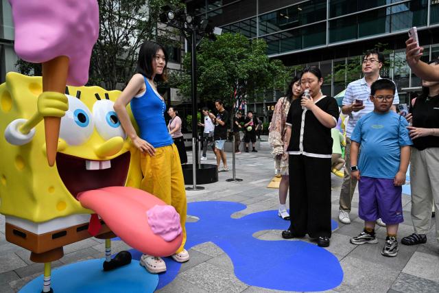 People pose next to figures from the Nickelodeon series SpongeBob SquarePants in a square in Shanghai on June 25, 2026. (Photo by Hector RETAMAL / AFP)