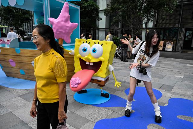 People pose next to figures from the Nickelodeon series SpongeBob SquarePants in a square in Shanghai on June 25, 2026. (Photo by Hector RETAMAL / AFP)