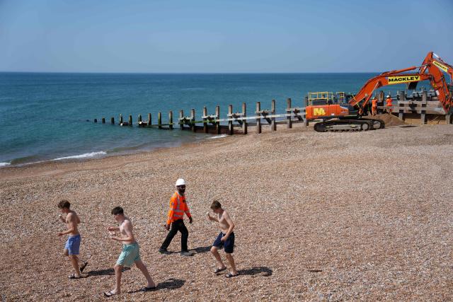 Children walk with ice creams as as work continues on the beach groynes, part of the coastal protection scheme in Hove, on the south coast of England on June 25, 2026, during a heatwave. The UK recorded its hottest ever June temperature on June 24 with the mercury rising to 36.1C in southern England, breaking the previous record of 35.6C set in 1976. (Photo by CARLOS JASSO / AFP)