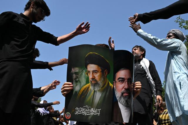 A Shia Muslim holds a poster with portraits of Iran's supreme leader Mojtaba Khamenei and late supreme leader Ayatollah Ali Khamenei (L) as mourners take part in a procession on the ninth day of the Islamic holy month of Muharram in Islamabad on June 25, 2026. (Photo by Aamir QURESHI / AFP)