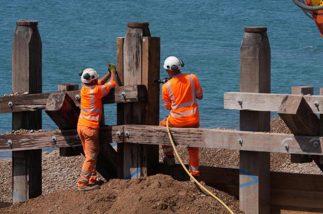 Workers stand in the sun as they work on beach groynes, part of the coastal protection scheme in Hove, on the south coast of England on June 25, 2026, during a heatwave. The UK recorded its hottest ever June temperature on June 24 with the mercury rising to 36.1C in southern England, breaking the previous record of 35.6C set in 1976. (Photo by CARLOS JASSO / AFP)