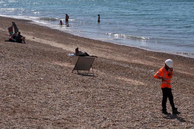 People enjoy the sea and the sun, as a worker working on the coastal protection scheme to improve the beach groynes, stands on the beach in Hove, on the south coast of England on June 25, 2026, during a heatwave. The UK recorded its hottest ever June temperature on June 24 with the mercury rising to 36.1C in southern England, breaking the previous record of 35.6C set in 1976. (Photo by CARLOS JASSO / AFP)