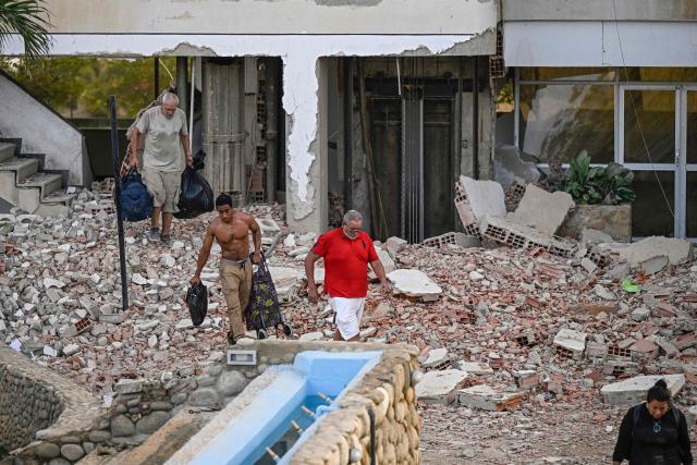 People carry their belongings out of a damaged building following an earthquake in Catia La Mar, La Guaira state, some 30km north-west of Caracas, on June 25, 2026. A twin earthquake that was Venezuela's largest in over a century has killed at least 164 people and destroyed multiple buildings near the capital, where residents searched on June 25 for missing relatives. (Photo by Federico PARRA / AFP)