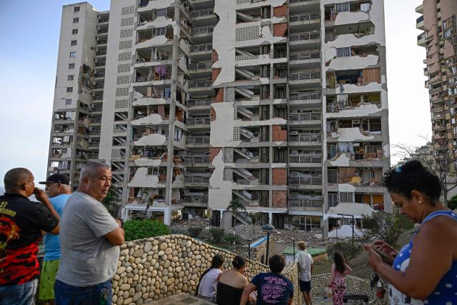 People stand before damaged apartment buildings following an earthquake in Catia La Mar, La Guaira state, some 30km north-west of Caracas, on June 25, 2026. A twin earthquake that was Venezuela's largest in over a century has killed at least 164 people and destroyed multiple buildings near the capital, where residents searched on June 25 for missing relatives. (Photo by Federico PARRA / AFP)