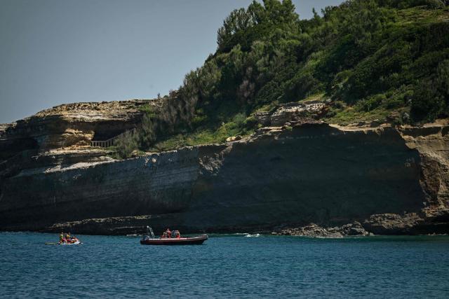 Firefighters search by boat at the base of the cliff from which a section collapsed near Miramar beach, killing one woman and leaving a diver missing, in Biarritz, south-western France, on June 25, 2026. The collapse came at around 8:20 pm (1820 GMT) near the Miramar beach, which was packed with swimmers seeking respite from a punishing heatwave. (Photo by Philippe LOPEZ / AFP)