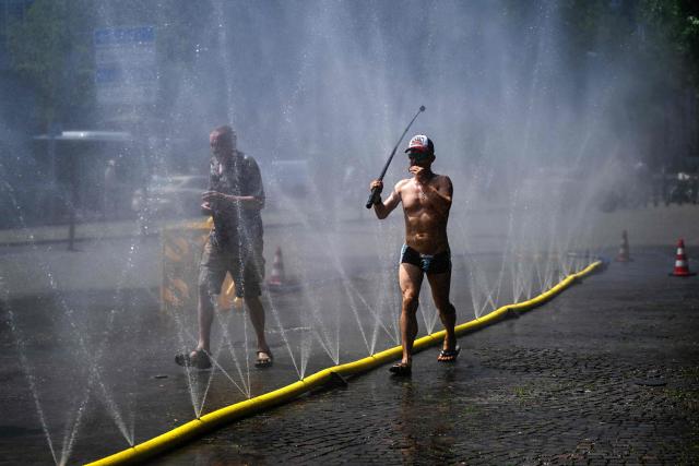 A man walks with a selfie stick past water hoses spilling water to provide relief from the summer heat as part of Colognes climate adaptation measures in Cologne, western Germany on June 25, 2026 during a heatwave in Europe. A heatwave sweeping Europe was starting to peak in Germany on June 25, 2026, with several open-air events cancelled and temperatures expected to top 40C through the weekend. Large parts of the country are already under "severe to extreme heat stress" with temperatures soaring to around 37C, the German Weather Service (DWD) said. (Photo by Ina FASSBENDER / AFP)