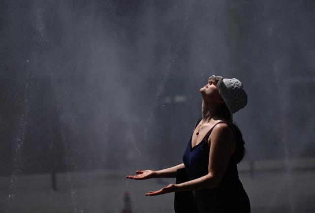 A woman cools down at water hoses spilling water to provide relief from the summer heat as part of Colognes climate adaptation measures in Cologne, western Germany on June 25, 2026 during a heatwave in Europe. A heatwave sweeping Europe was starting to peak in Germany on June 25, 2026, with several open-air events cancelled and temperatures expected to top 40C through the weekend. Large parts of the country are already under "severe to extreme heat stress" with temperatures soaring to around 37C, the German Weather Service (DWD) said. (Photo by Ina FASSBENDER / AFP)