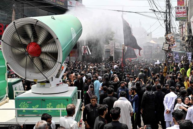 A mist cannon sprays water as Shia Muslims take part in a religious procession on the ninth day of the Islamic holy month of Muharram in Lahore on June 25, 2026. (Photo by Arif ALI / AFP)