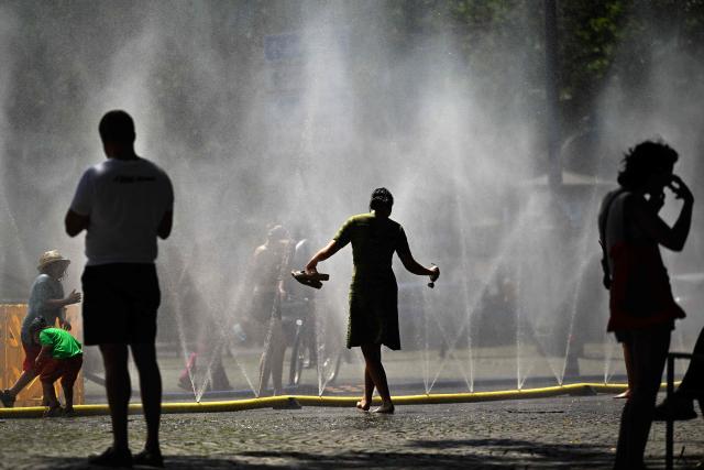 TOPSHOT - People stand near over water hoses spilling water to provide relief from the summer heat as part of Colognes climate adaptation measures in Cologne, western Germany on June 25, 2026 during a heatwave in Europe. A heatwave sweeping Europe was starting to peak in Germany on June 25, 2026, with several open-air events cancelled and temperatures expected to top 40C through the weekend. Large parts of the country are already under "severe to extreme heat stress" with temperatures soaring to around 37C, the German Weather Service (DWD) said. (Photo by Ina FASSBENDER / AFP)