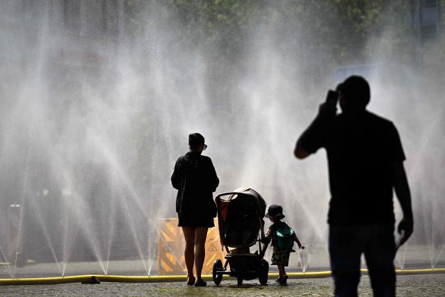People stand near over water hoses spilling water to provide relief from the summer heat as part of Colognes climate adaptation measures in Cologne, western Germany on June 25, 2026 during a heatwave in Europe. A heatwave sweeping Europe was starting to peak in Germany on June 25, 2026, with several open-air events cancelled and temperatures expected to top 40C through the weekend. Large parts of the country are already under "severe to extreme heat stress" with temperatures soaring to around 37C, the German Weather Service (DWD) said. (Photo by Ina FASSBENDER / AFP)
