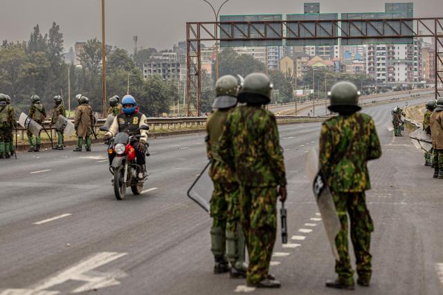 A man rides a motorbike past Kenyan police officers as they guard a roadblock ahead of demonstrations planned to mark the second anniversary of the deadly June 2024 youth-led anti-Finance Bill protests, which saw demonstrators storm Parliament, in Nairobi on June 25, 2026. Kenyan police put on a massive show of force on June 25 in a bid to prevent protests marking two years since a landmark Gen Z uprising. Thousands of Kenyans took to the streets in June 2024 against economic hardship and corruption, eventually storming parliament to force the cancellation of new taxes. (Photo by SIMON MAINA / AFP)