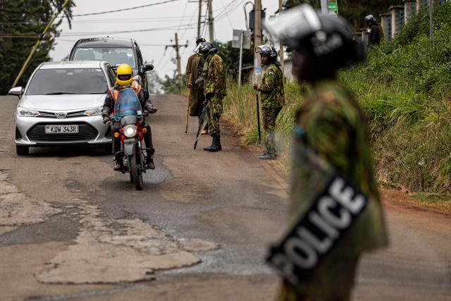 A man rides a motorbike past Kenyan police officers as they guard a roadblock ahead of demonstrations planned to mark the second anniversary of the deadly June 2024 youth-led anti-Finance Bill protests, which saw demonstrators storm Parliament, in Nairobi on June 25, 2026. Kenyan police put on a massive show of force on June 25 in a bid to prevent protests marking two years since a landmark Gen Z uprising. Thousands of Kenyans took to the streets in June 2024 against economic hardship and corruption, eventually storming parliament to force the cancellation of new taxes. (Photo by SIMON MAINA / AFP)