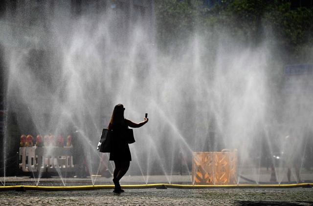 A woman takes a photo of water hoses spilling water to provide relief from the summer heat as part of Colognes climate adaptation measures in Cologne, western Germany on June 25, 2026 during a heatwave in Europe. A heatwave sweeping Europe was starting to peak in Germany on June 25, 2026, with several open-air events cancelled and temperatures expected to top 40C through the weekend. Large parts of the country are already under "severe to extreme heat stress" with temperatures soaring to around 37C, the German Weather Service (DWD) said. (Photo by Ina FASSBENDER / AFP)