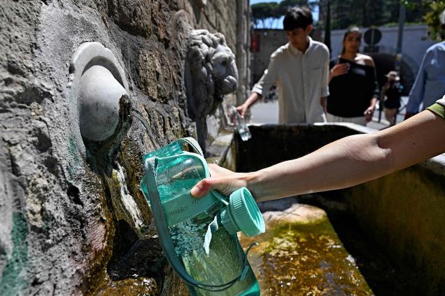 A woman fills a bottle with water at a public fountain during a heatwave, in Rome on June 25, 2026. (Photo by Andreas SOLARO / AFP)