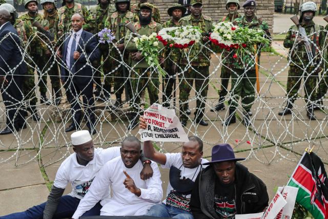 Activists stage a sit down near barbed-wire barrier set up to prevent them from gaining access to parliament precincts where they planned to lay flowers during demonstrations to mark the second anniversary of the deadly June 2024 youth-led anti-Finance Bill protests, which saw demonstrators storm Parliament, in Nairobi on June 25, 2026. Kenyan police put on a massive show of force on June 25 in a bid to prevent protests marking two years since a landmark Gen Z uprising. Thousands of Kenyans took to the streets in June 2024 against economic hardship and corruption, eventually storming parliament to force the cancellation of new taxes. (Photo by Tony KARUMBA / AFP)