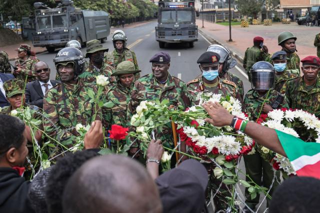 Kenyan police officers watch as activists place flowers on barbed-wire barrier set up to prevent them from gaining access to parliament precincts to lay floweres during demonstrations to mark the second anniversary of the deadly June 2024 youth-led anti-Finance Bill protests, which saw demonstrators storm Parliament, in Nairobi on June 25, 2026. Kenyan police put on a massive show of force on June 25 in a bid to prevent protests marking two years since a landmark Gen Z uprising. Thousands of Kenyans took to the streets in June 2024 against economic hardship and corruption, eventually storming parliament to force the cancellation of new taxes. (Photo by Tony KARUMBA / AFP)