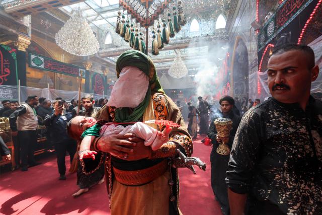 A Shia Muslim historical re-enactor walks with an infant child during a mourning procession near the Shrine of Imam Abbas in Iraq's holy city of Karbala on June 25, 2026 at the peak of Ashura, a 10-day period commemorating the seventh century killing of Prophet Mohammed's grandson Imam Hussein. (Photo by AHMAD AL-RUBAYE / AFP)