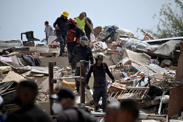 Rescue workers walk across the rubble of collapsed buildings during search efforts following an earthquake in Catia La Mar, La Guaira state, about 30 km northwest of Caracas, on June 25, 2026. A twin earthquake that was Venezuela's largest in over a century has killed at least 164 people and destroyed multiple buildings near the capital, where residents searched on June 25 for missing relatives. (Photo by Juan BARRETO / AFP)